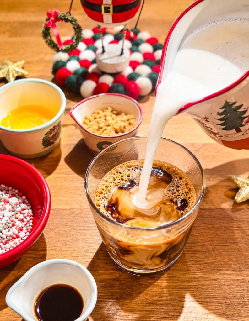 Pouring warm, frothy milk into espresso to make a homemade sugar cookie latte.