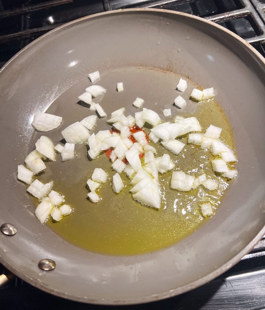 Diced white onions sautéing in olive oil in a skillet for Halloween monster tacos.
