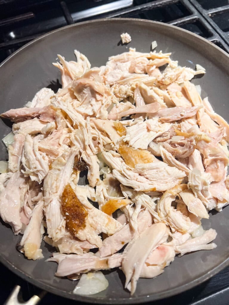 Shredded rotisserie chicken added to a skillet with sautéed onions and olive oil for Halloween monster tacos.